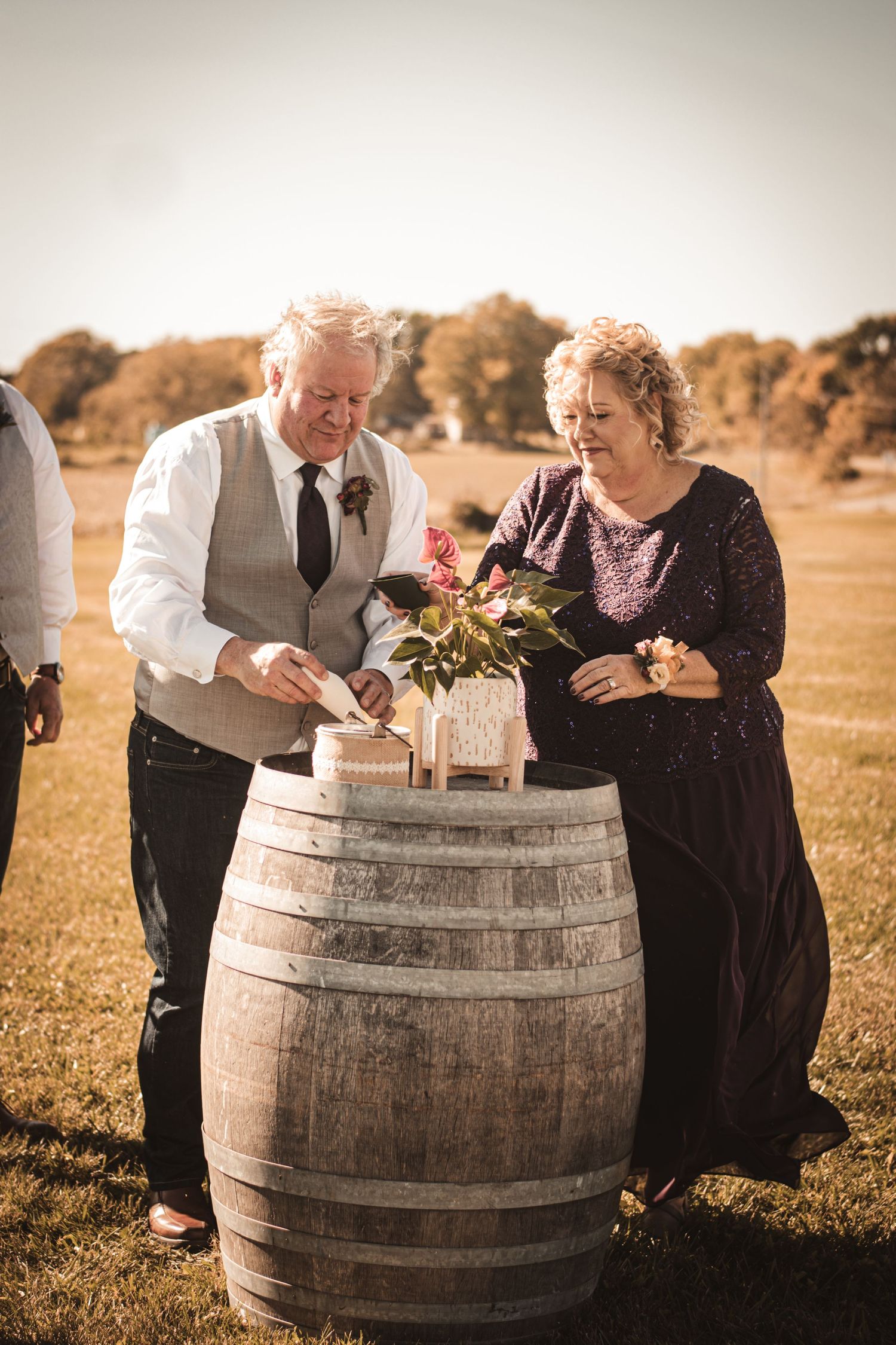 Wedding party members arrange decorations on wooden barrel during outdoor ceremony.