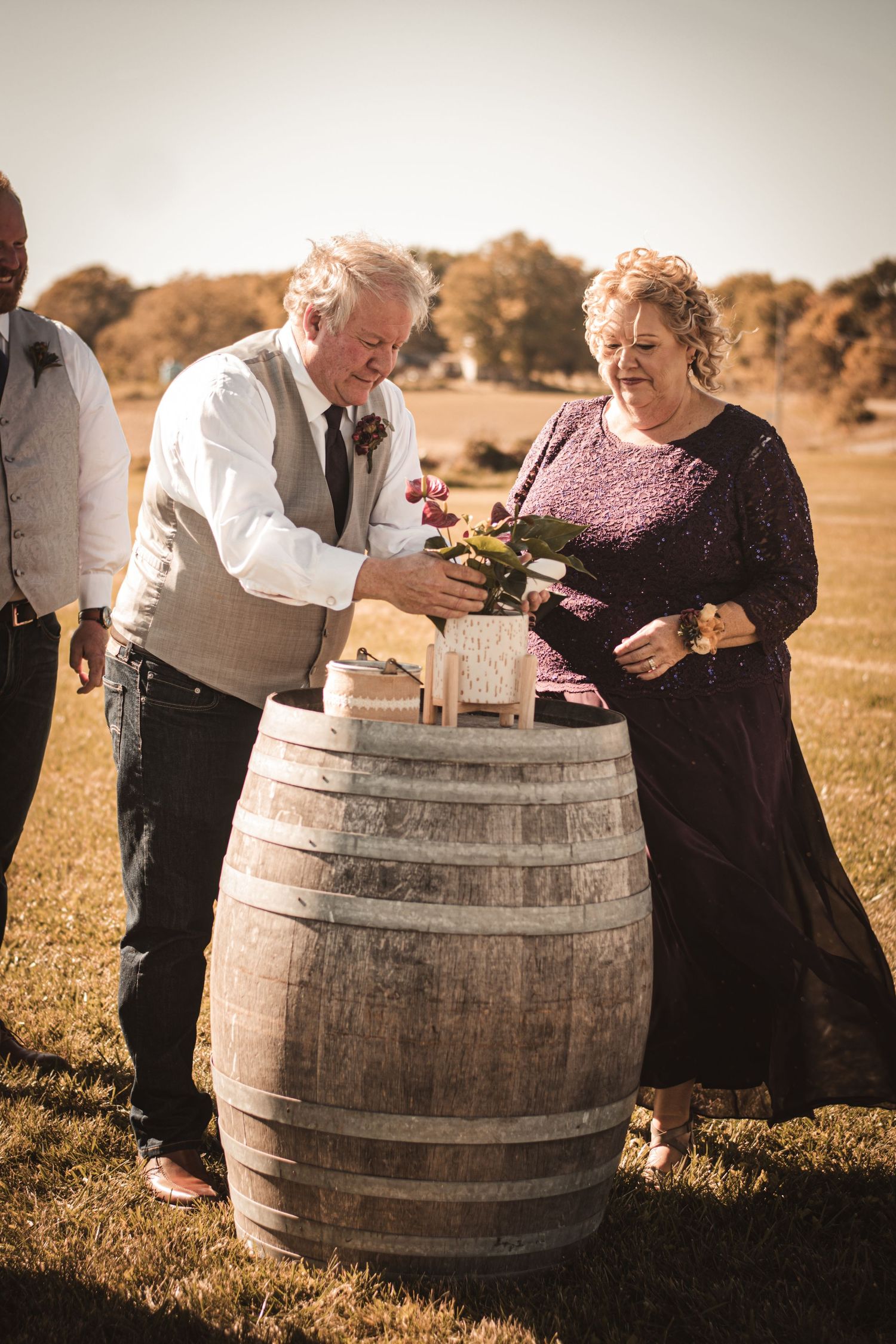 Wedding guests interact around rustic barrel display at outdoor autumn ceremony.