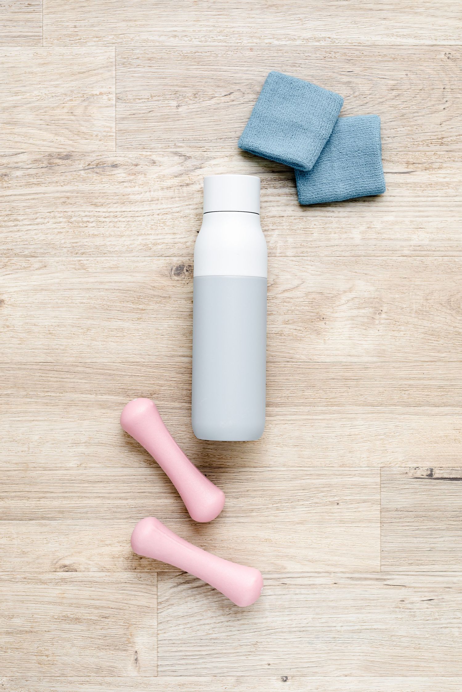 Pale blue water bottle on wooden floor with blue sweatbands and pink weights. Fitness, healthy lifestyle, exercise
