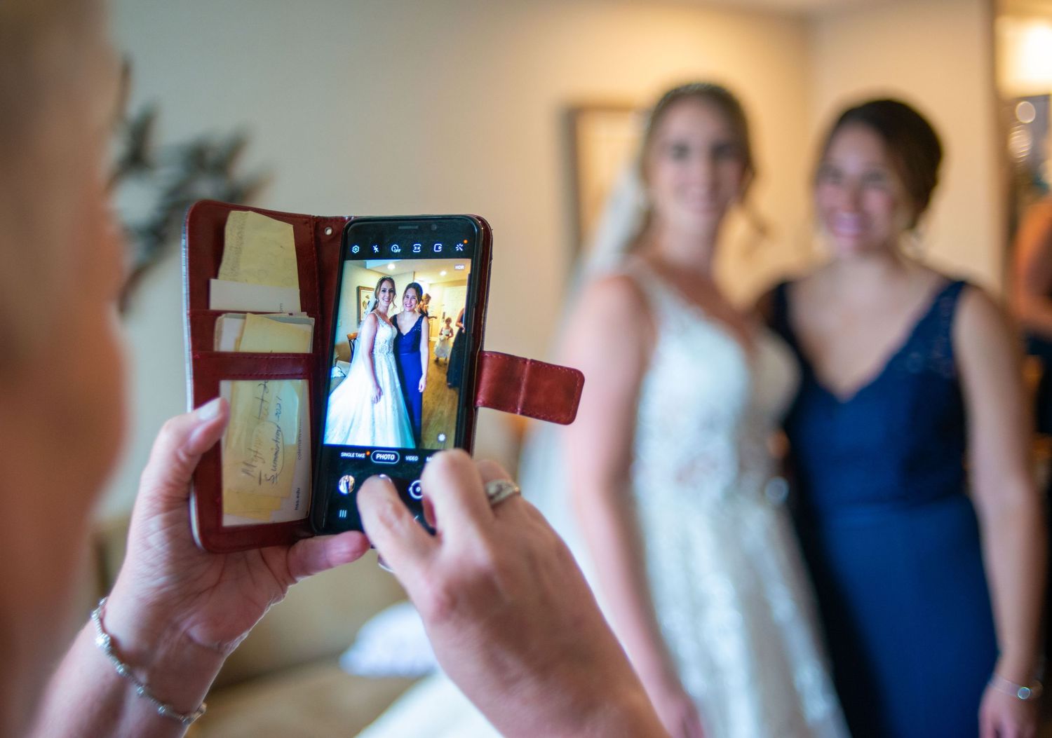 Someone taking photo of bride and bridesmaid on smartphone during wedding preparations.