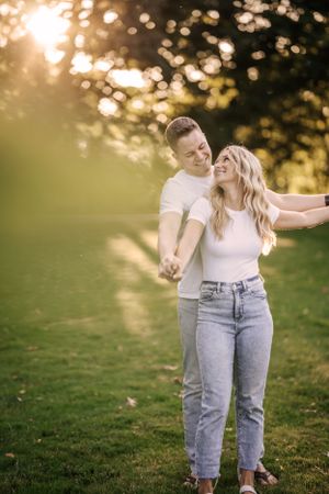 A playful couple embraces in a sunny park during golden hour.