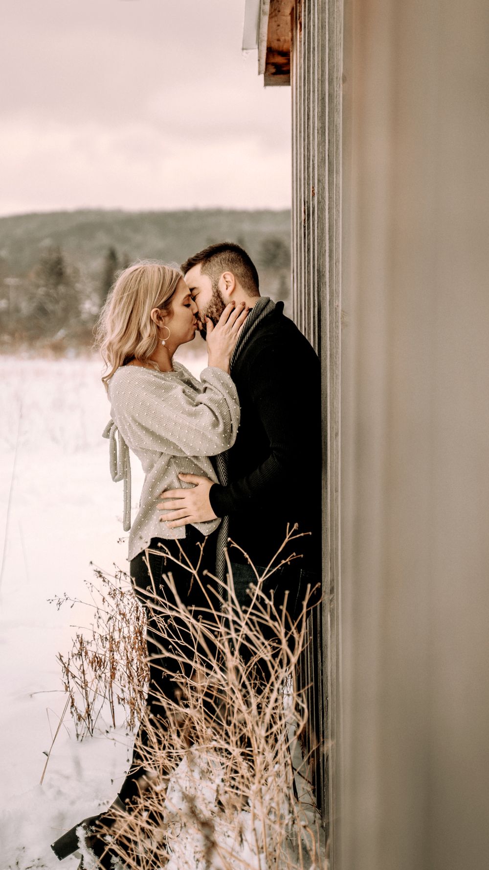 An intimate winter portrait of a couple sharing a tender moment in the doorway of a rustic building.