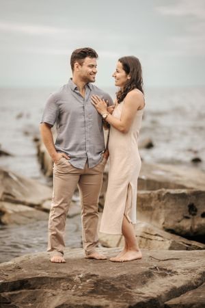 A couple shares an intimate moment while standing on coastal rocks by the ocean.
