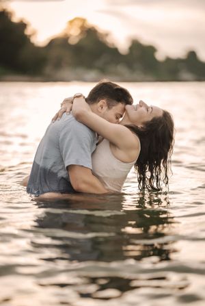 Romantic couple embraces in golden sunset waters with intimate pose and sunlit glow.
