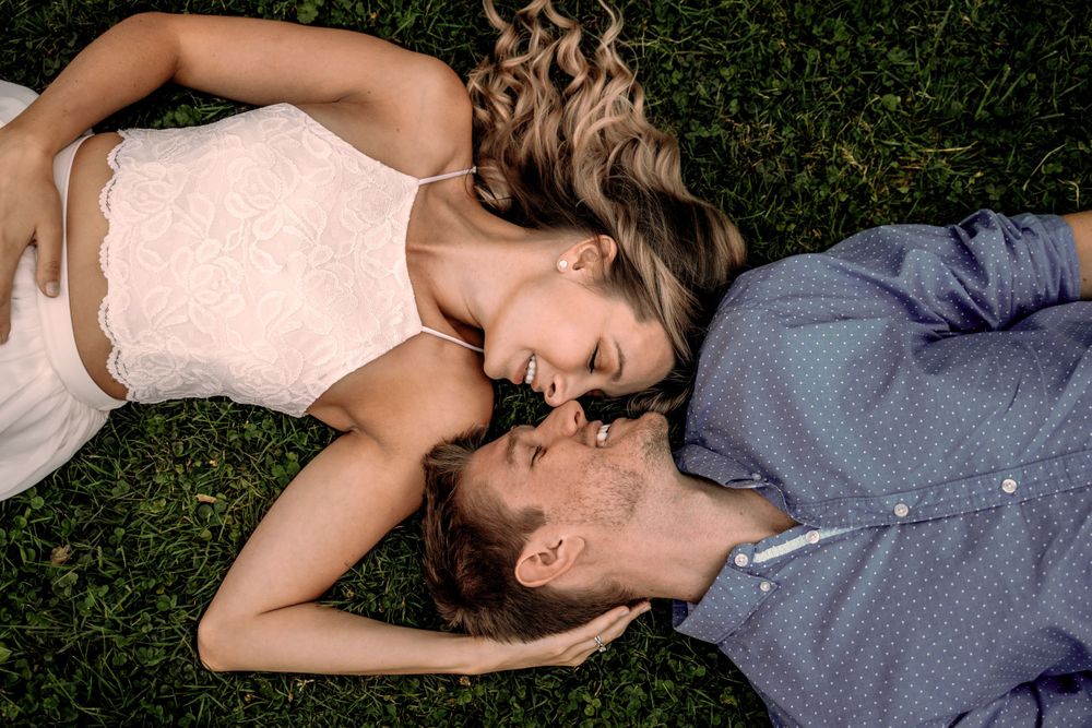 A couple lying on grass together sharing an intimate moment outdoors.