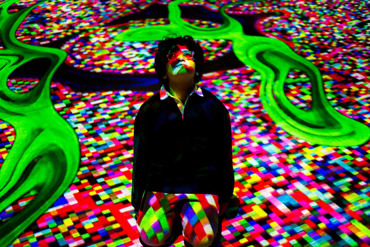 A figure stands amid a colorful digital art installation with neon green patterns and multicolored lights.