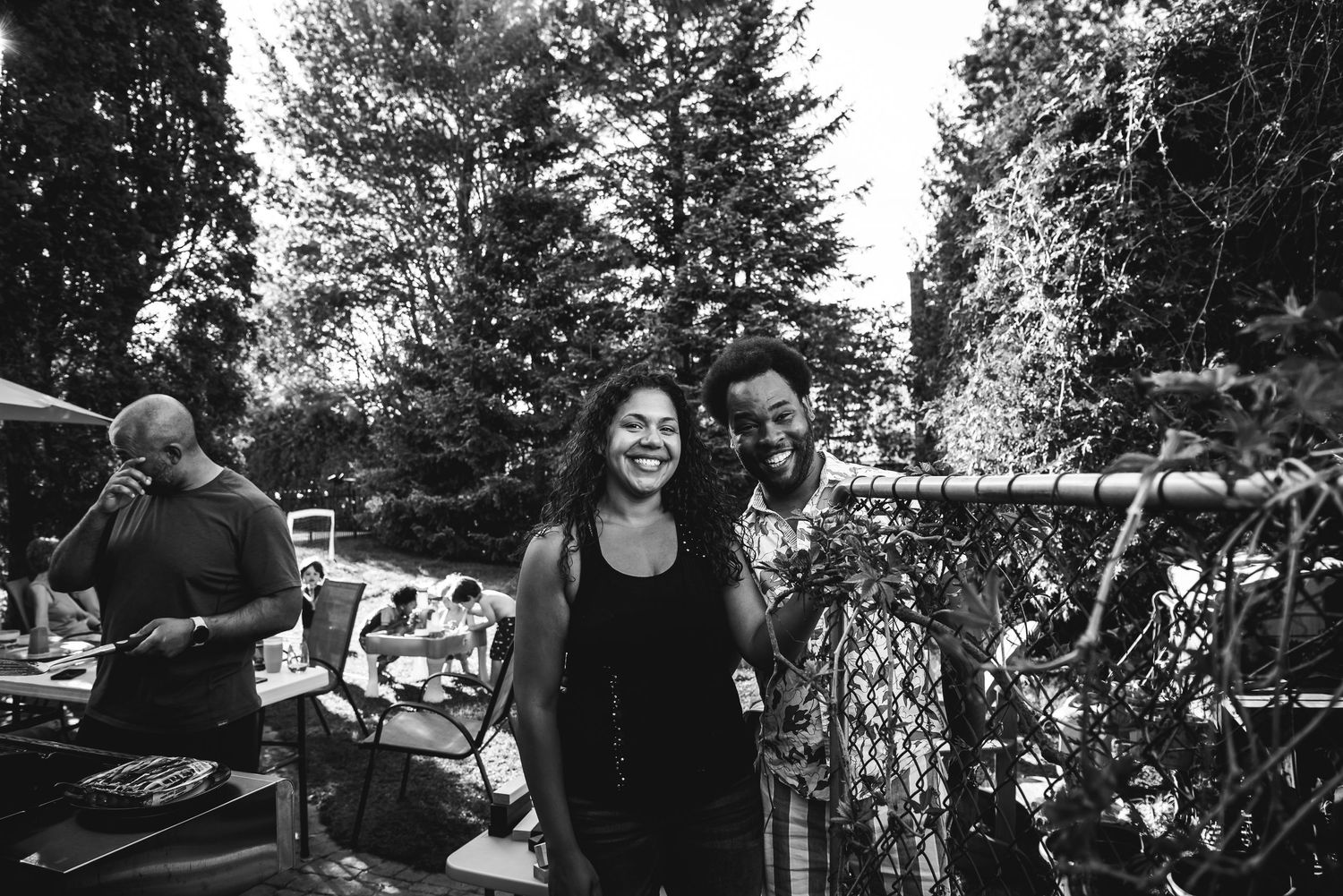 BW image of a black man and woman smiling at the camera from behind a chain gate.