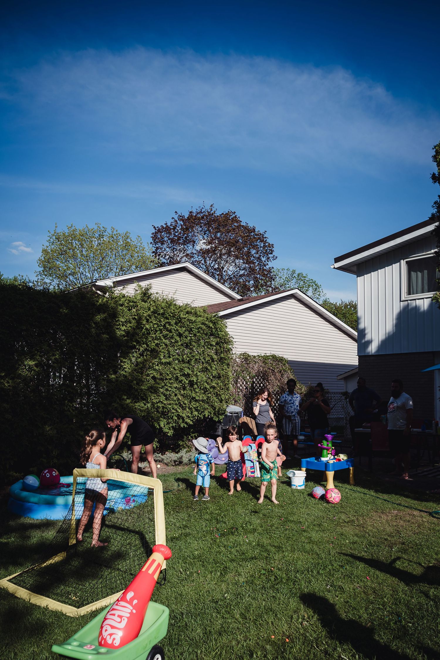 Backyard bbq scene of a bunch of children playing on green grass.