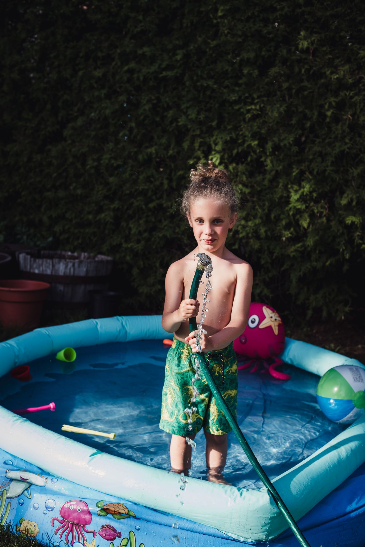 Colour image of a young white boy standing in a blue pool playing with a water hose.