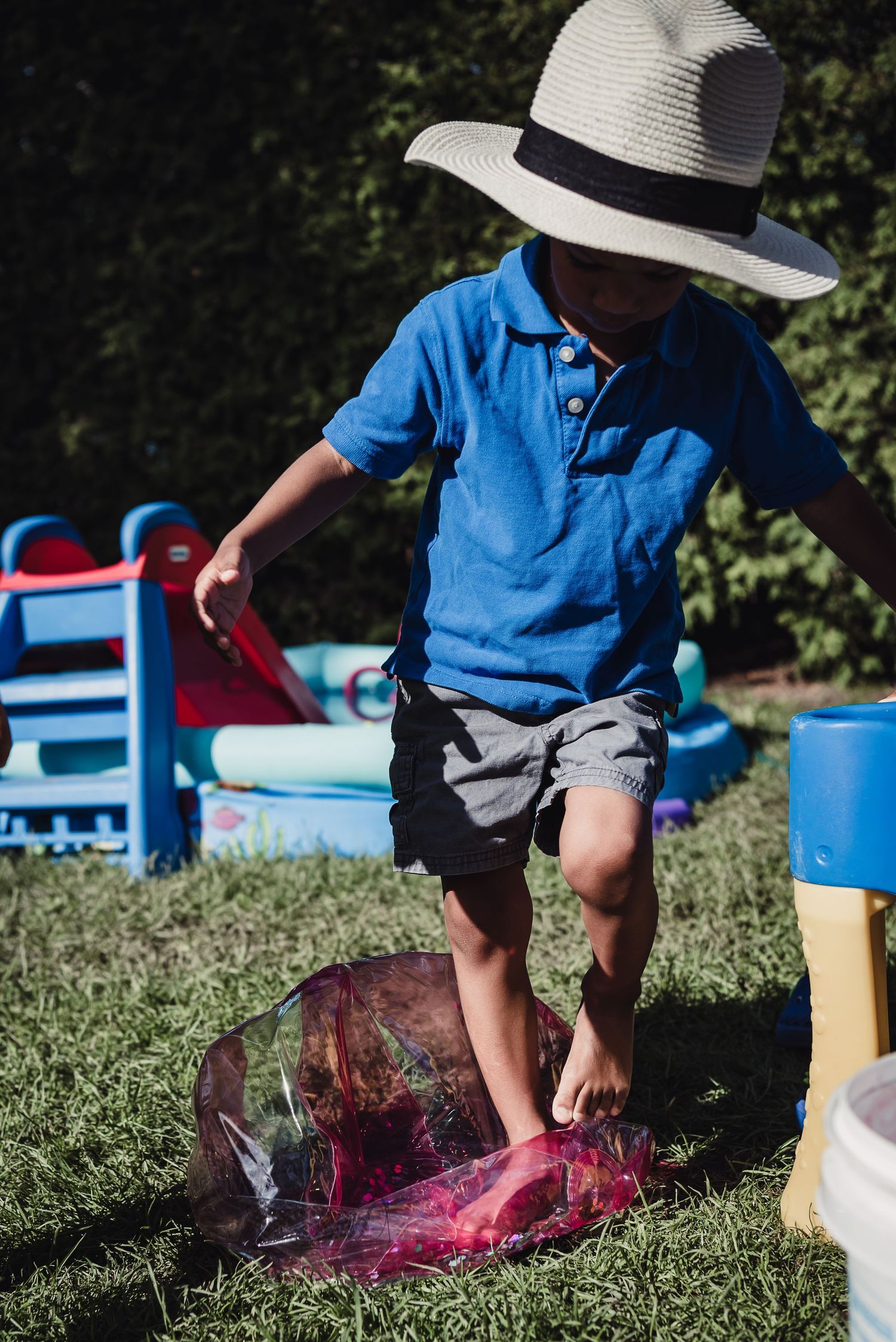A young black boy stands on a squishy ball at a backyard bbq.