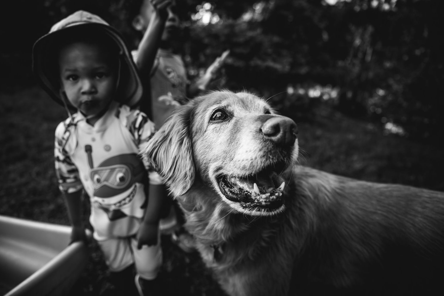 BW image of a boy standing beside a golden retriever.
