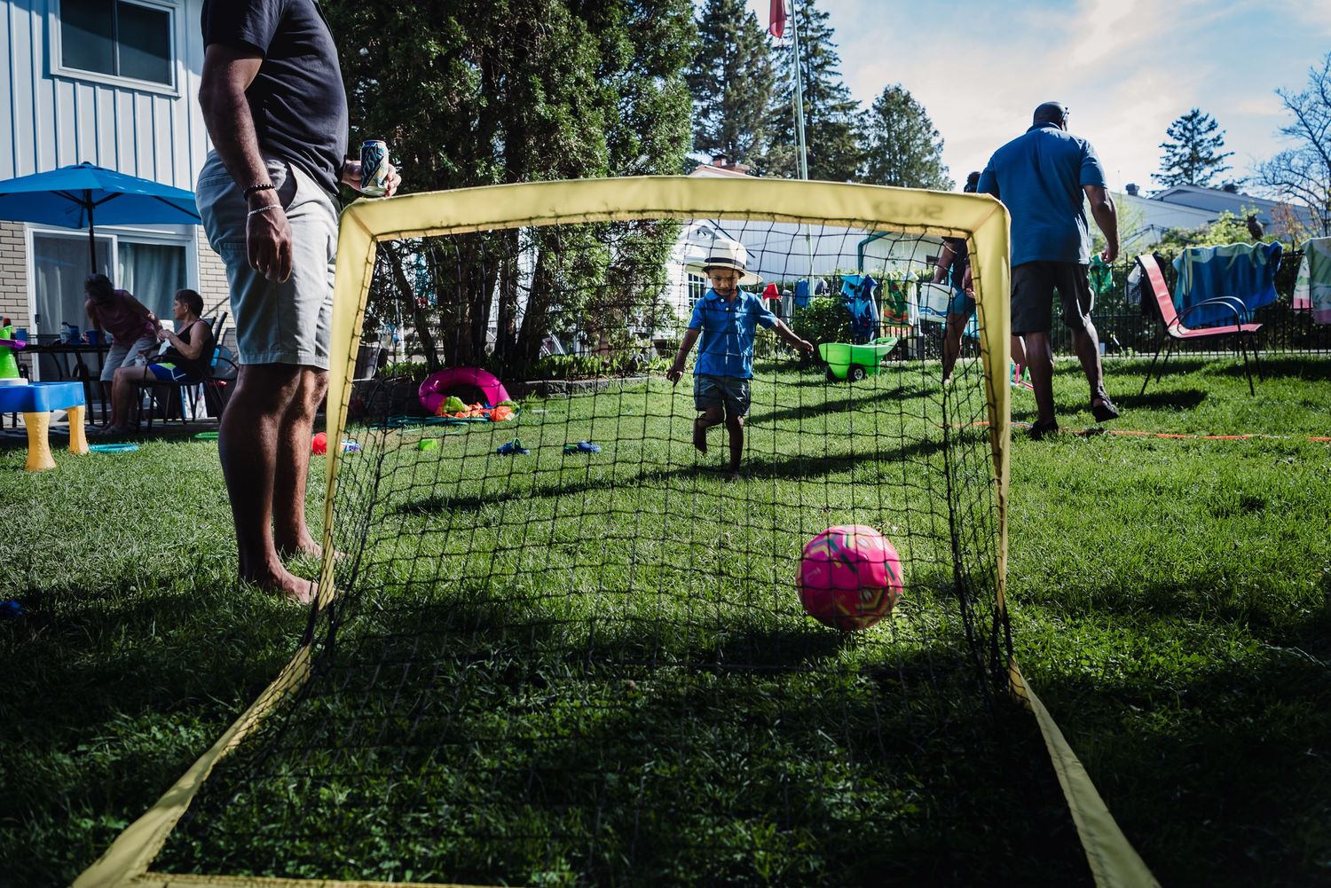 Colour image taken behind a net as a young child kicks a red ball into it.