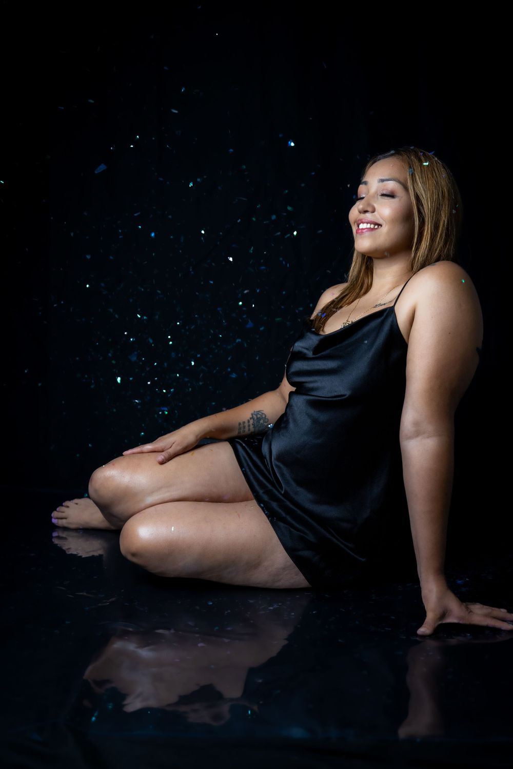 Woman poses gracefully in black satin dress against sparkly dark background.