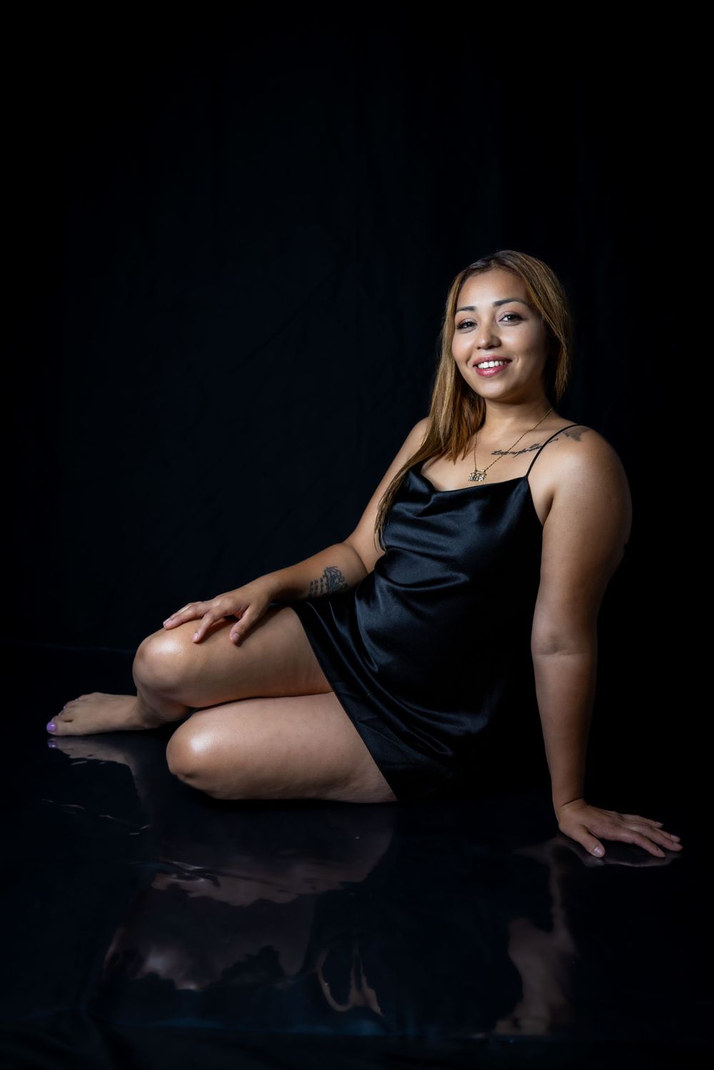 Elegant posed portrait on reflective surface with black backdrop.
