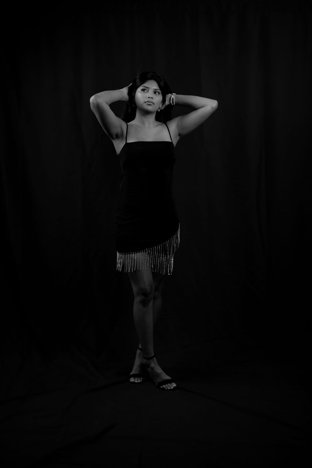 An artistic black and white portrait of a woman in a fringed dress striking a pose.