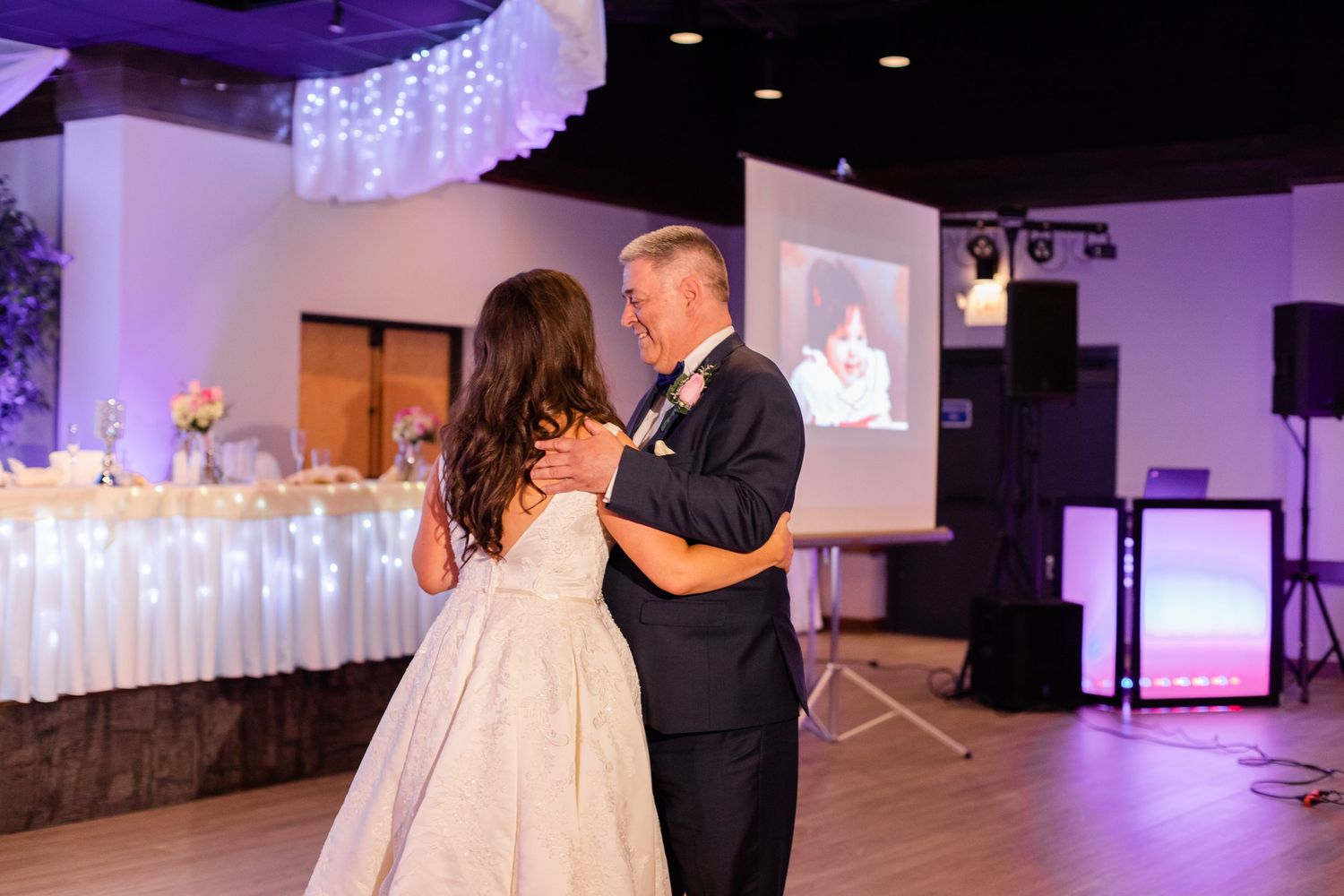 A couple shares an intimate dance moment under purple lighting at their wedding reception.