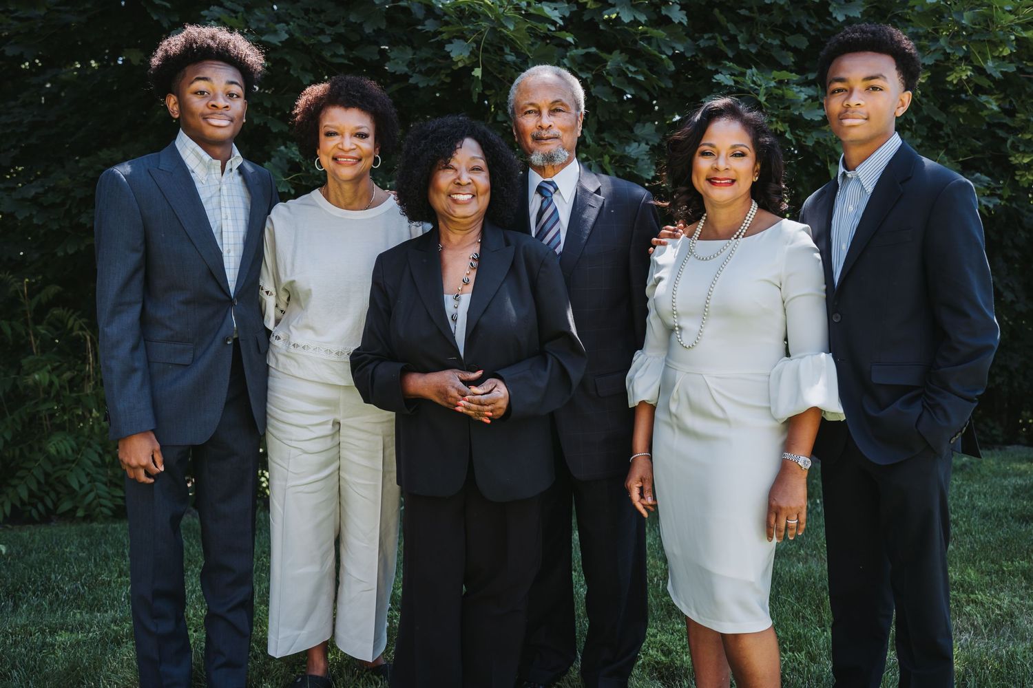 Formal family portrait of six people in elegant attire posing outdoors in garden setting.