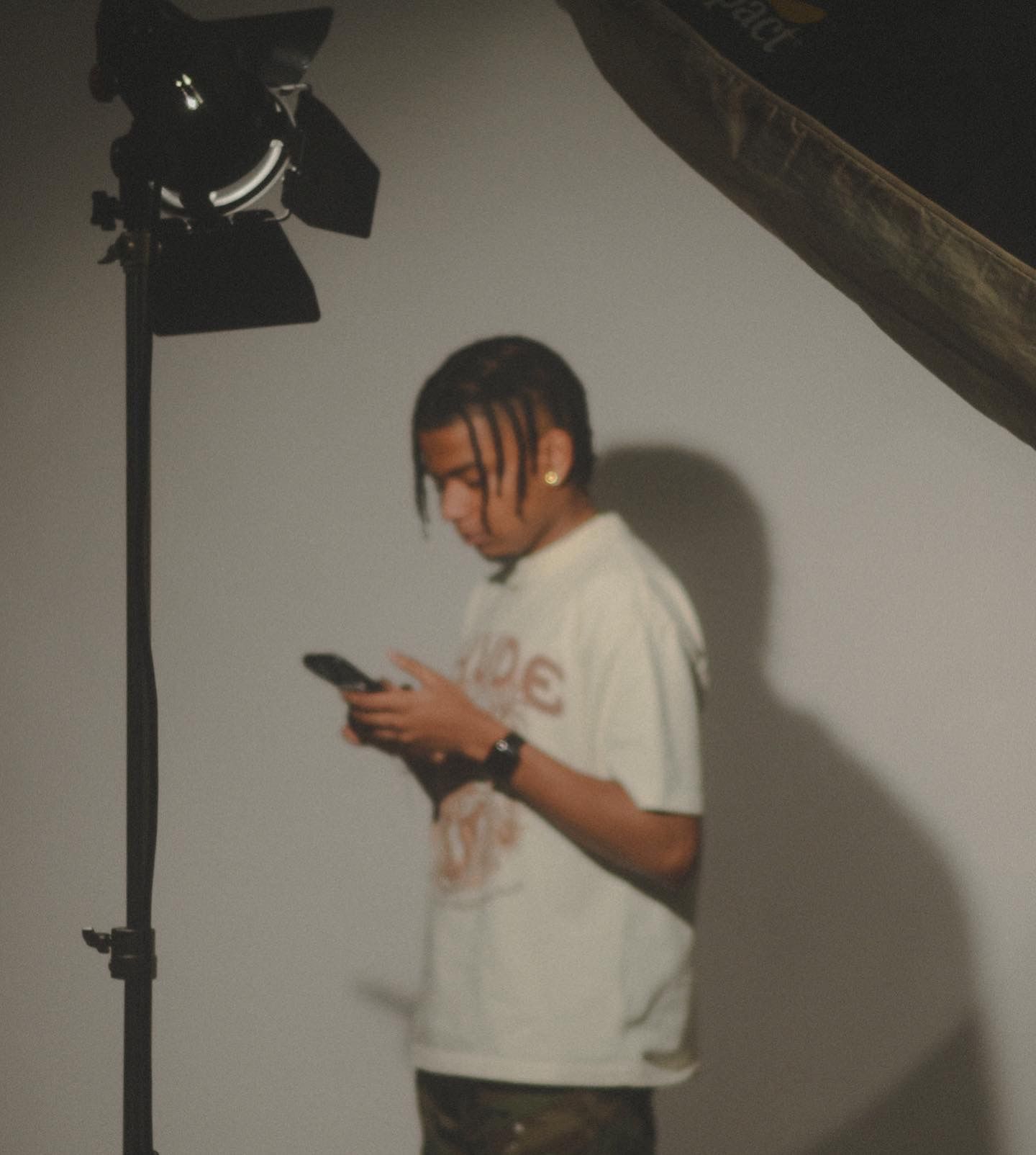 Studio photo of someone in a white t-shirt looking at their phone next to a professional light stand.