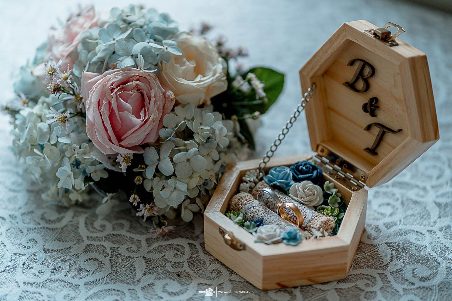 Wedding ring box with initials alongside delicate pink and blue floral arrangement.