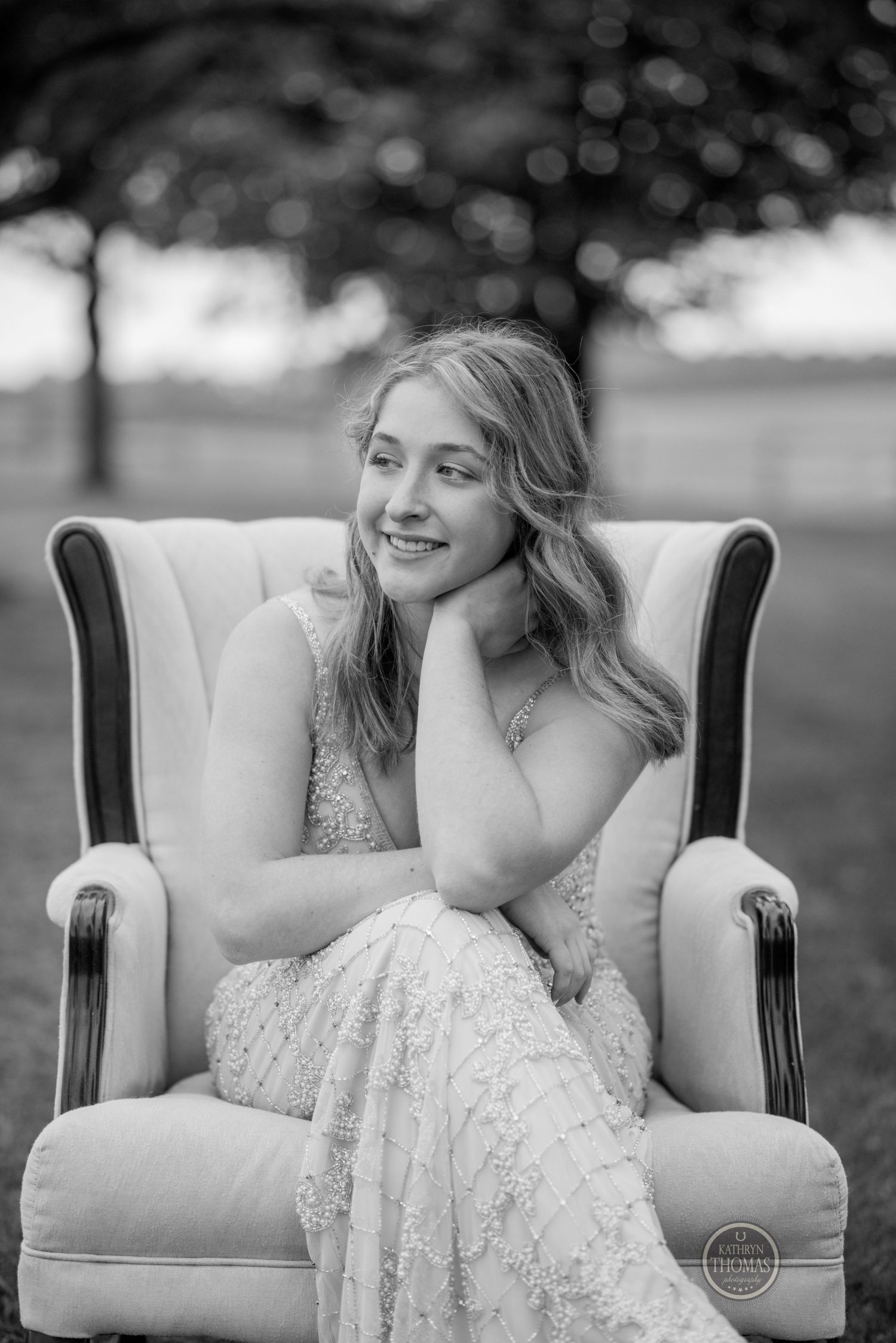 Black and white portrait of a woman in an elegant dress posing in a vintage armchair.