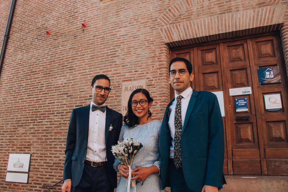 A wedding party of three people poses together outside a vintage brick building.