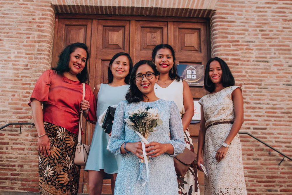 A group of five women in formal attire pose together on steps of a brick building.