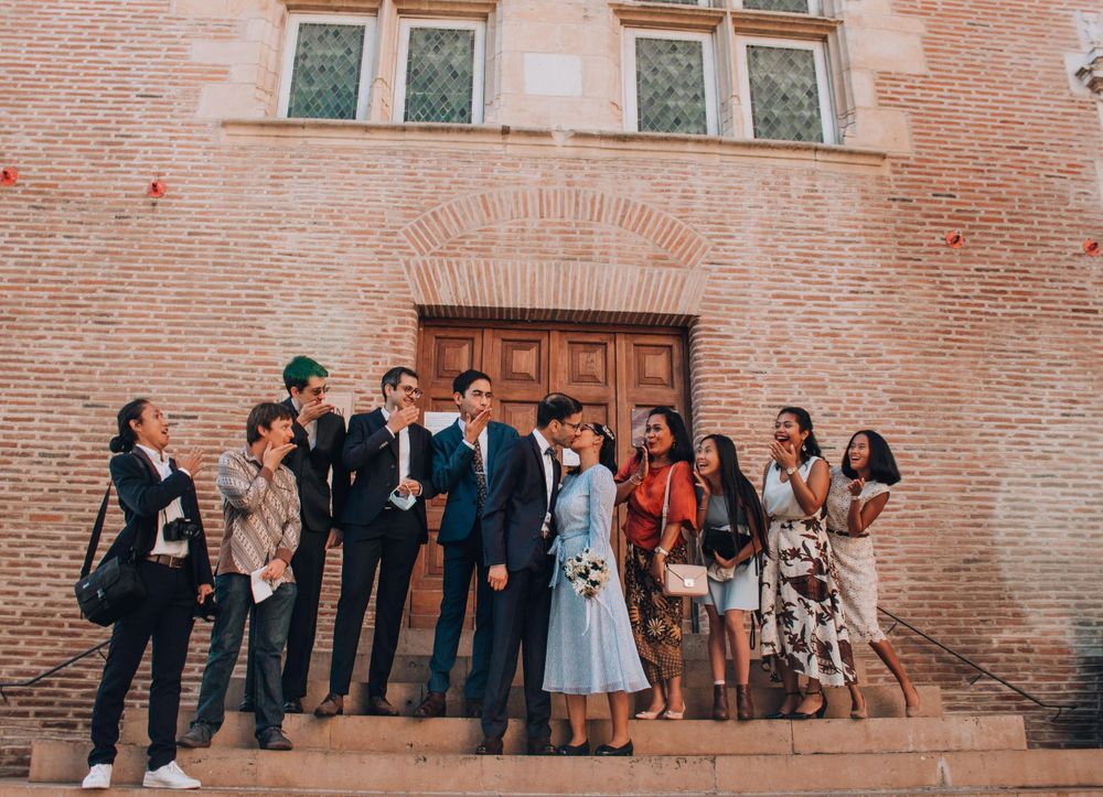 A wedding party poses together outside a historic brick building with wooden doors.