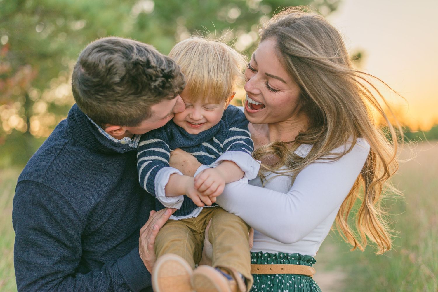 mom and dad smile and kiss their baby, holding him between them