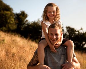 Young girl photographed on her father's shoulders in warm light