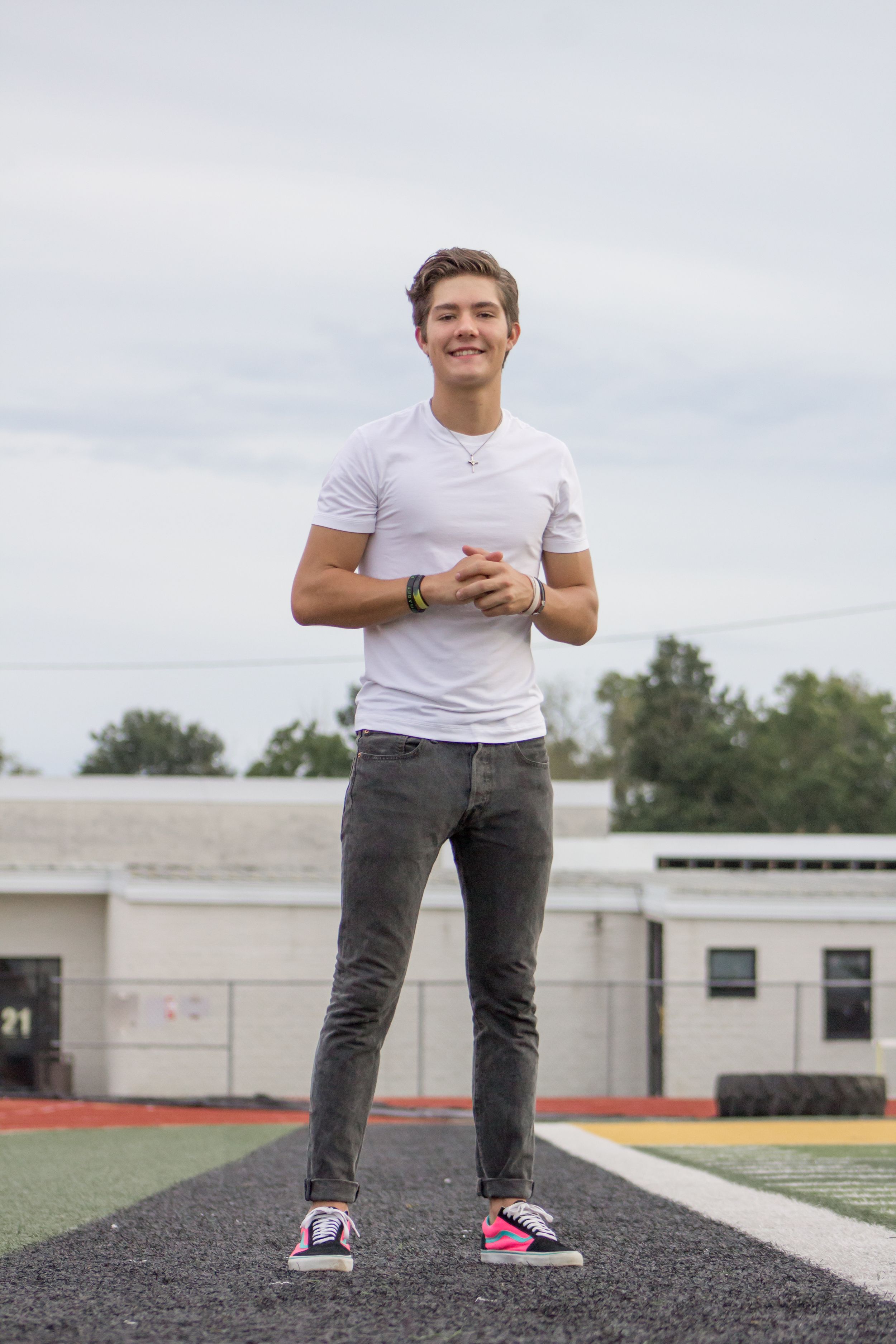 Smiling teenage boy in white t-shirt and gray jeans stands on a school athletic track.