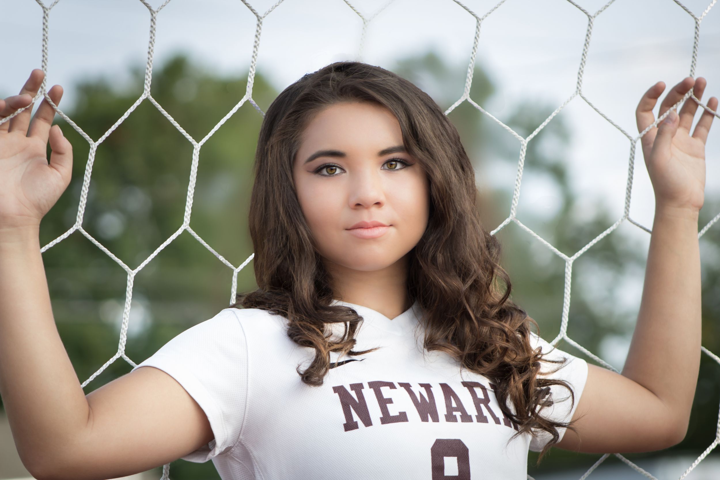 Teen girl in Newark soccer jersey posing at goal net for senior portrait.