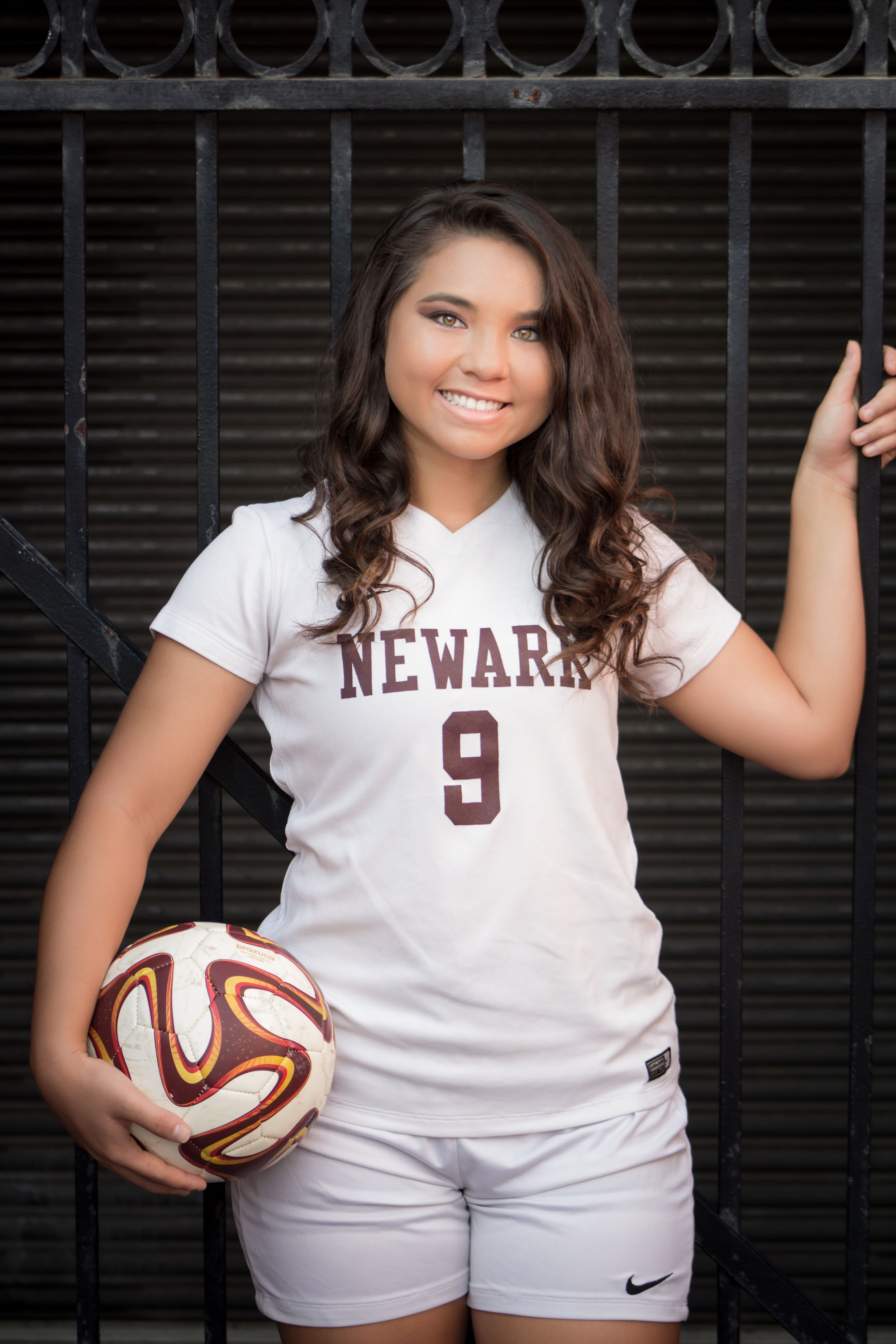Smiling girl in Newark number 9 soccer jersey holding ball for senior photo.