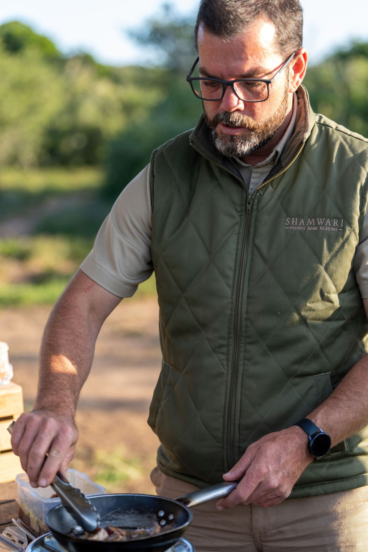 Person in green vest preparing food outdoors at sunset.