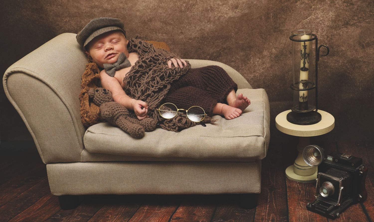 A sleeping infant lies on a brown leather couch in a rustic setting.