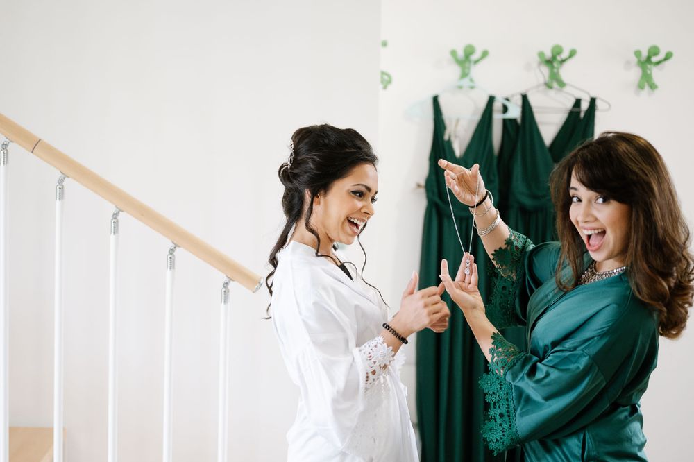 Two women in robes celebrating and laughing with green decor in background.