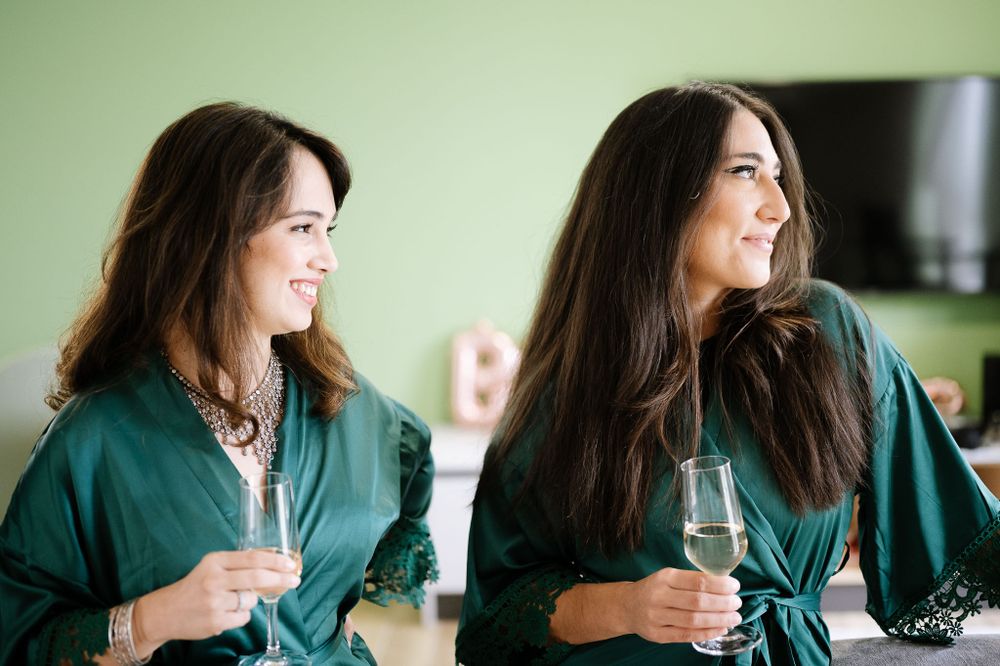 Two women in green robes sharing drinks and laughing together.