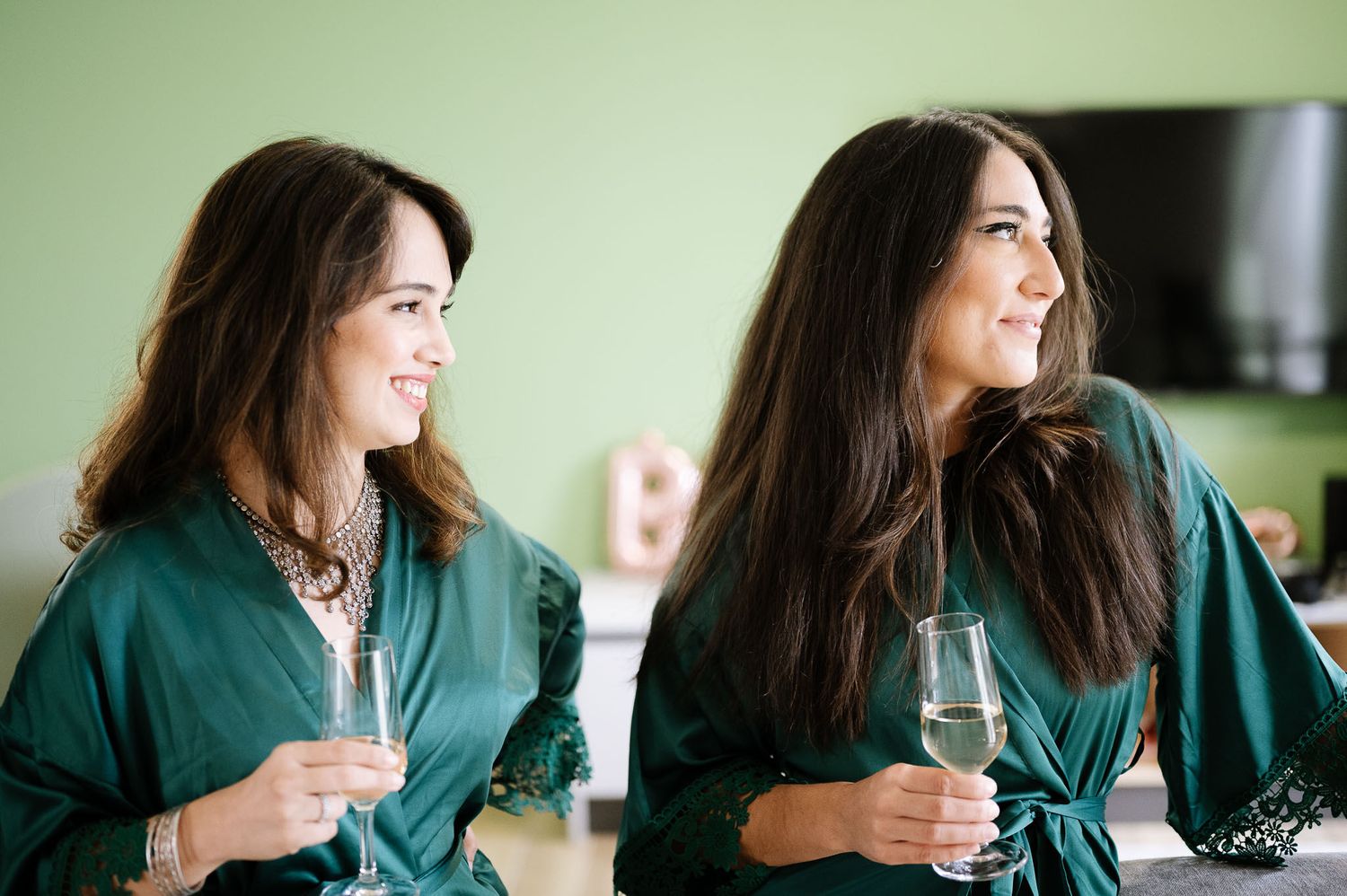 Two women in green robes sharing drinks and laughing together.