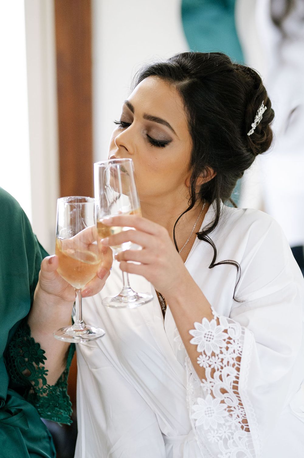 Woman in white robe sipping champagne during wedding preparations.