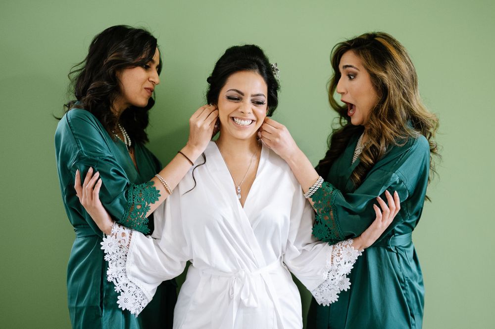 Three women in teal and white robes sharing a joyful moment against a mint green wall.