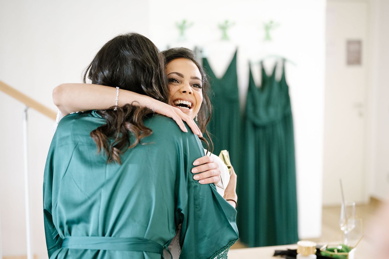 Two women in emerald green robes share an emotional hug during wedding preparations.