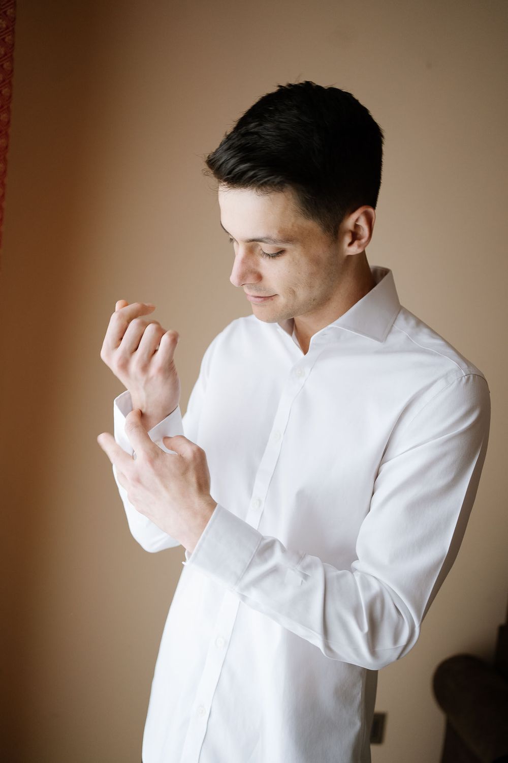 Man in white dress shirt adjusts his cuffs while getting ready.