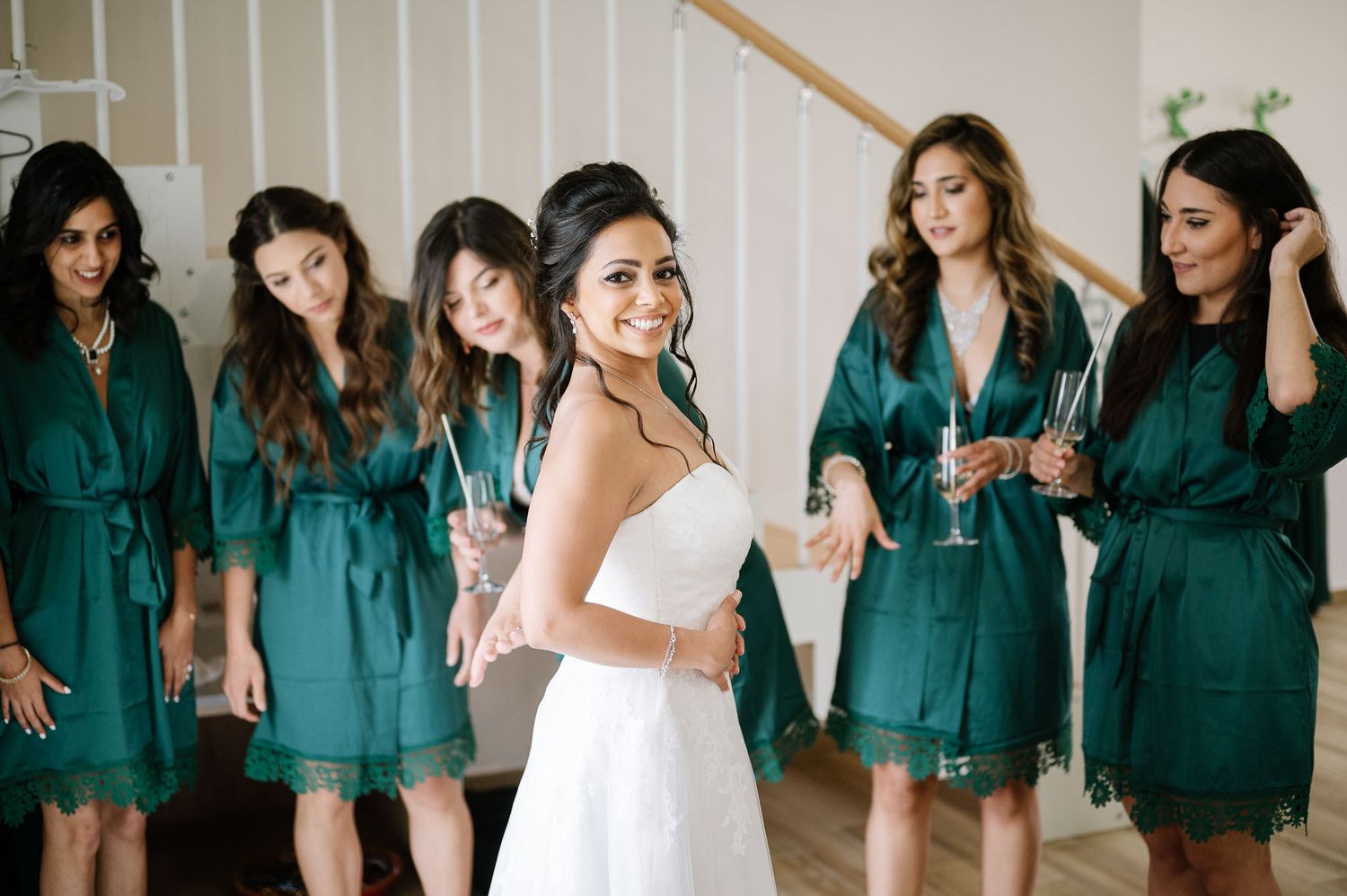 Bride in white dress poses with bridesmaids wearing matching teal robes.