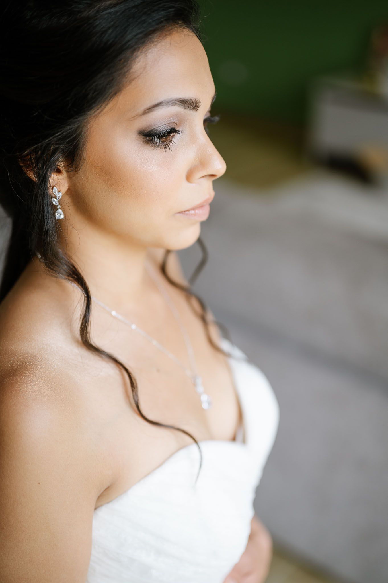 Close-up profile of bride wearing delicate necklace and strapless wedding gown.