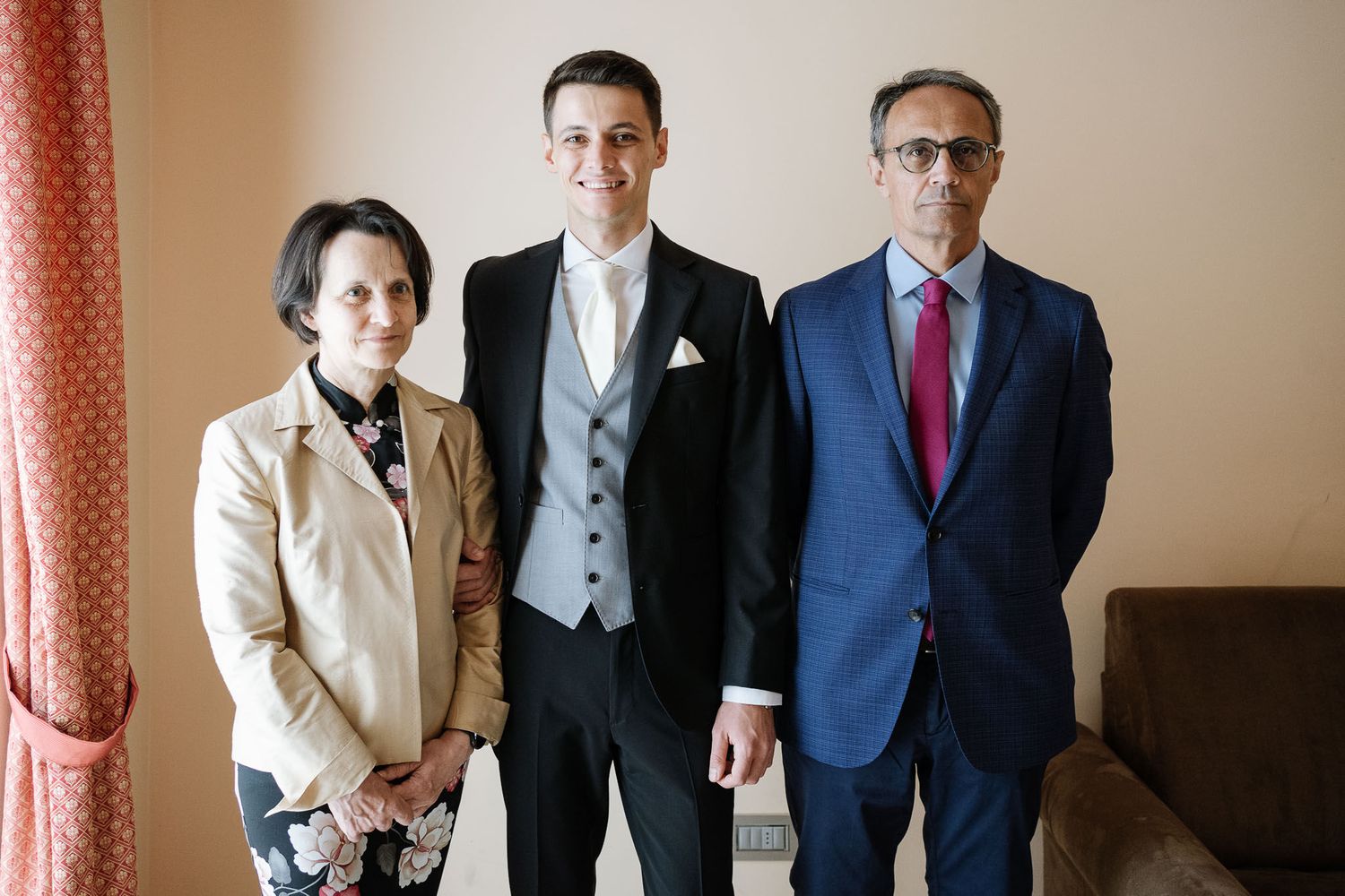 Wedding party portrait featuring groom in tuxedo with two formally dressed guests.