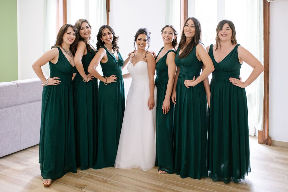 Bride in white dress poses with bridesmaids wearing elegant emerald green gowns.