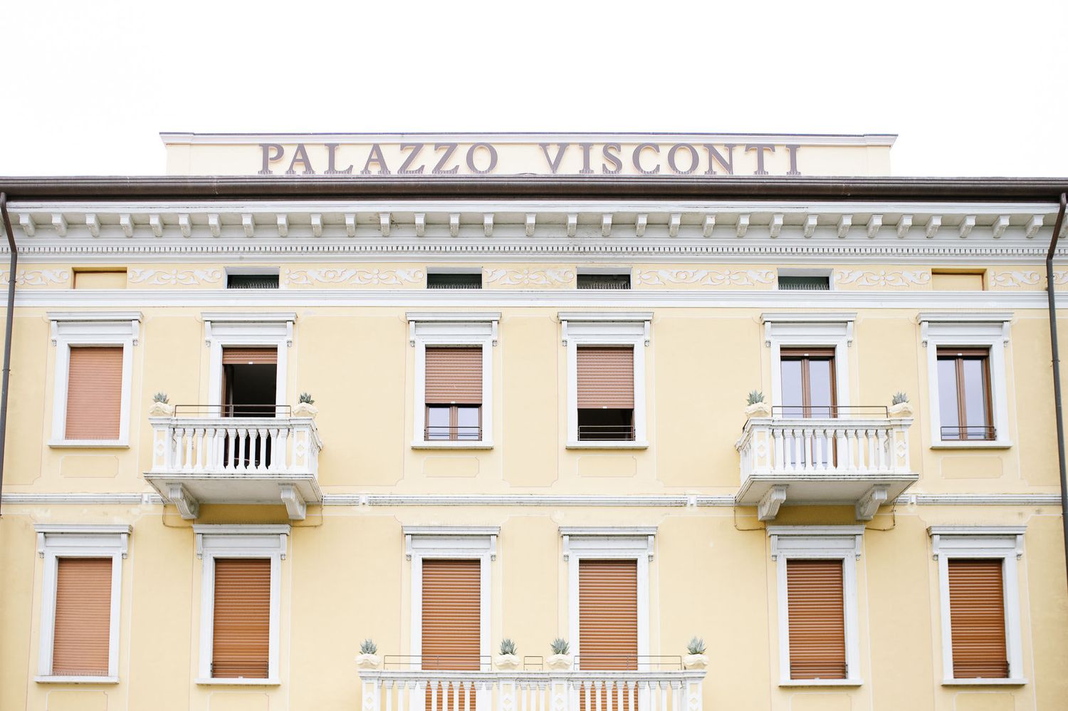 Yellow facade of Palazzo Visconti building with ornate balconies and classical architecture.