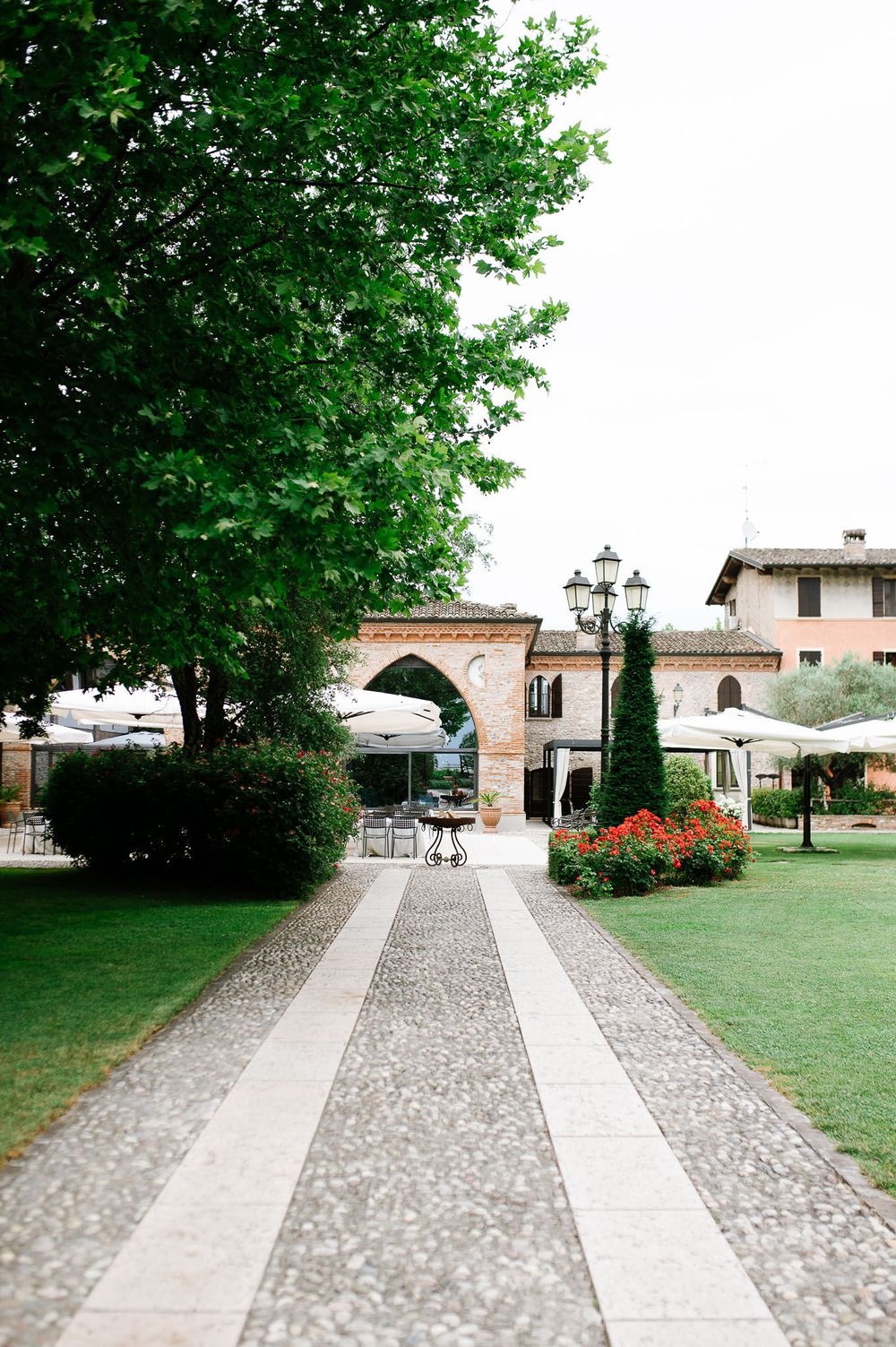 Stone pathway leading through manicured garden with arch and ornate lampposts.
