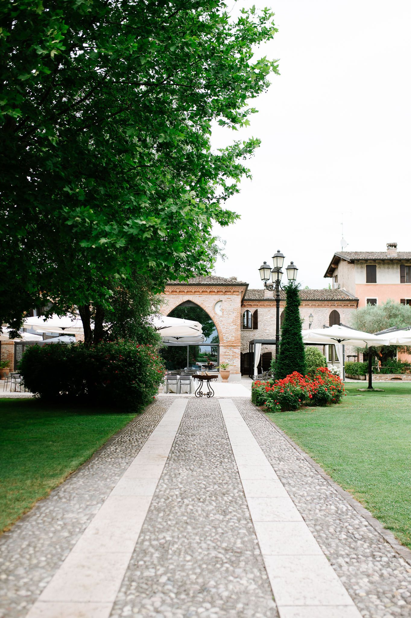 Stone pathway leading through manicured garden with arch and ornate lampposts.