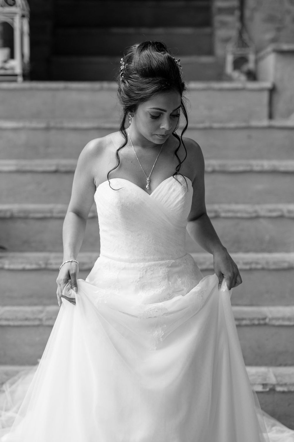 Black and white portrait of bride in strapless wedding gown on stone steps.