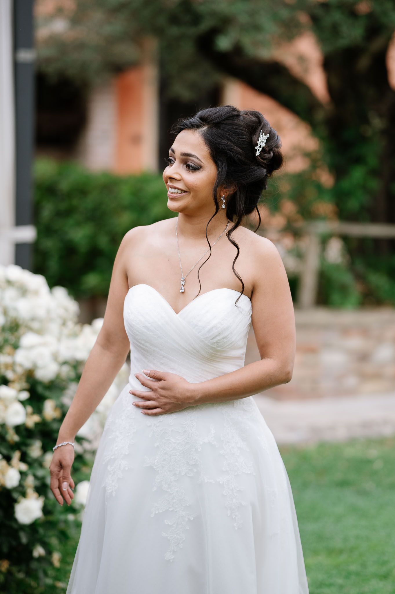 Elegant bride in a white strapless wedding gown poses in a garden setting with natural styling.